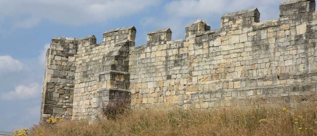 a large fortress wall lined at the bottom with tall grass